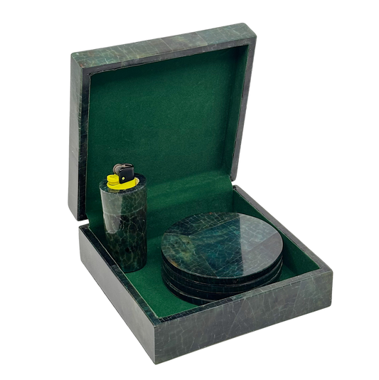 A gift box with a green velvet interior containing a lighter and a coaster, with a marble-like pattern on the interior surfaces.