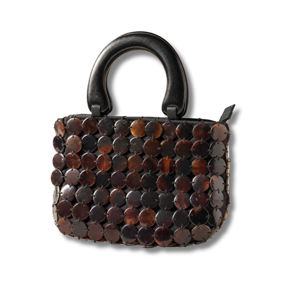 The Marlowe top-handle bag, a mosaic of polished black tab shell discs in cognac, amber and ebony, with a carved wooden handle.