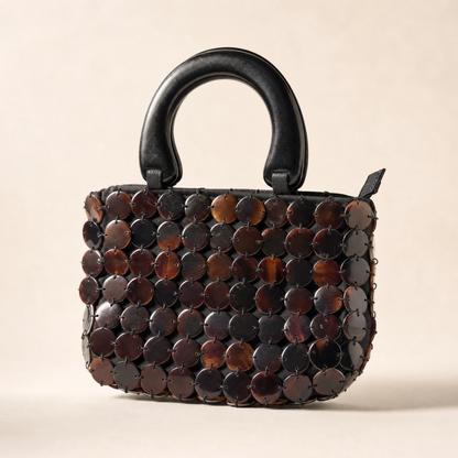 Close view of the Marlowe bag's shell mosaic, round black tab discs catching the light in tones of cognac, amber and deep ebony.